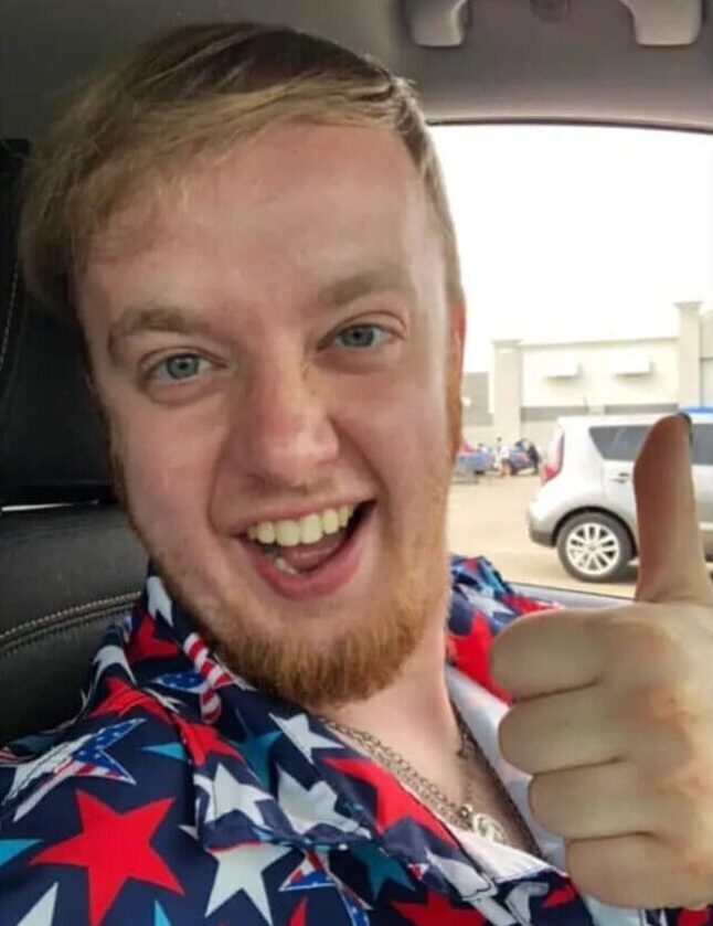 a smiling selfie of convicted cyberstalker Luke Wenke wearing a patriotic shirt and sitting in a vehicle
